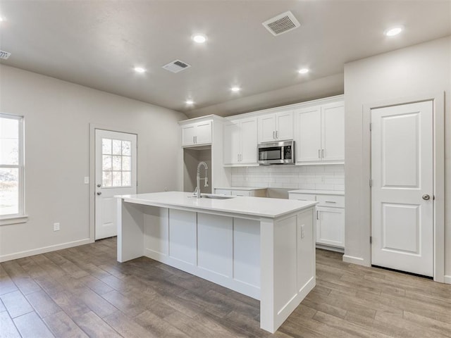 kitchen featuring white cabinetry, decorative backsplash, sink, and a center island with sink