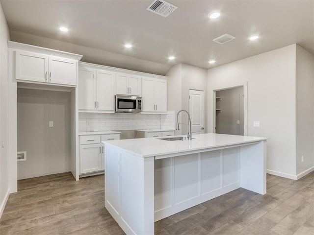 kitchen with sink, a center island with sink, white cabinets, and light hardwood / wood-style flooring