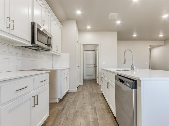 kitchen with white cabinetry, backsplash, stainless steel appliances, a center island with sink, and light hardwood / wood-style flooring