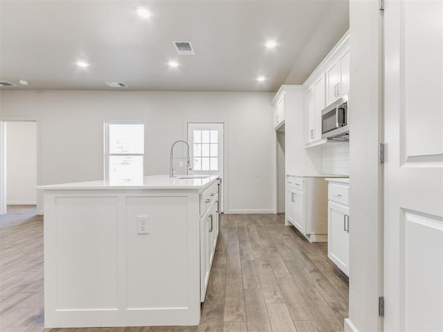 kitchen with a kitchen island with sink, sink, white cabinets, and light wood-type flooring