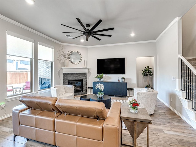 living room with crown molding, a stone fireplace, light hardwood / wood-style floors, and ceiling fan