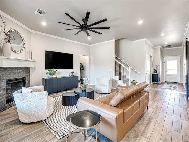 living room featuring crown molding, a stone fireplace, ceiling fan, and light wood-type flooring