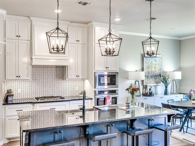 kitchen featuring an island with sink, appliances with stainless steel finishes, pendant lighting, and dark stone counters