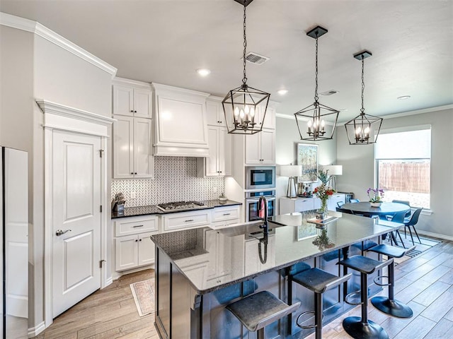 kitchen featuring appliances with stainless steel finishes, white cabinetry, a spacious island, decorative light fixtures, and dark stone counters