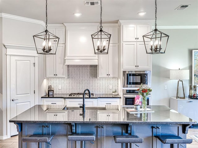 kitchen with hanging light fixtures, a kitchen island with sink, a breakfast bar area, and white cabinets