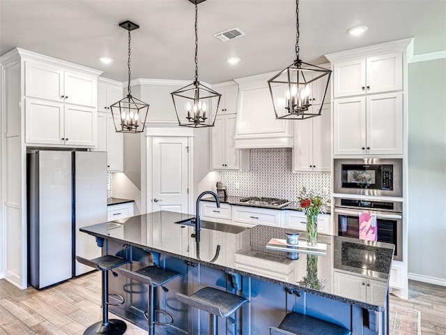 kitchen with a kitchen island with sink, decorative light fixtures, stainless steel appliances, and white cabinets