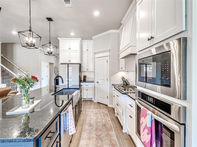 kitchen with white cabinetry, stainless steel appliances, hanging light fixtures, and a center island with sink