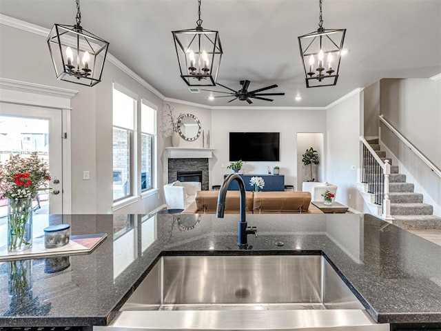 kitchen with dark stone countertops, a stone fireplace, pendant lighting, and ornamental molding