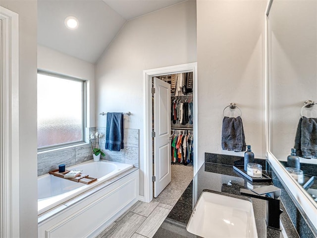 bathroom featuring a tub to relax in, lofted ceiling, and sink