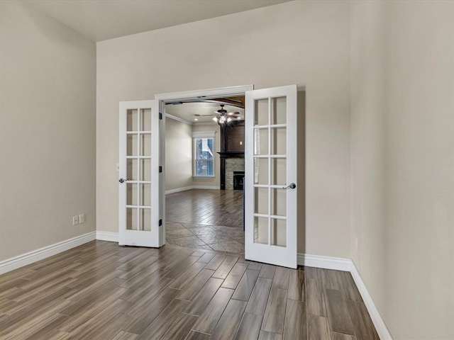 empty room featuring wood tiled floor, a fireplace, baseboards, and french doors