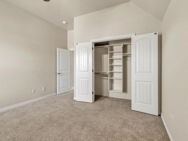 unfurnished bedroom featuring lofted ceiling, a closet, baseboards, and carpet flooring