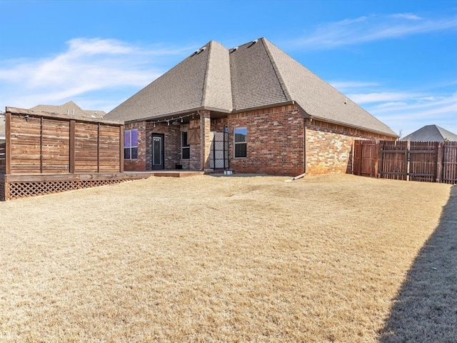 back of property with a yard, brick siding, a shingled roof, and fence