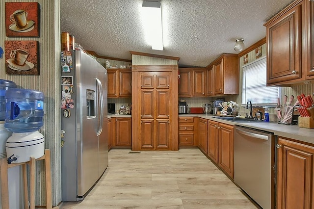 kitchen with appliances with stainless steel finishes, sink, a textured ceiling, and light hardwood / wood-style floors