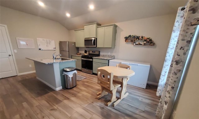 kitchen with an island with sink, light stone counters, wood finished floors, vaulted ceiling, and stainless steel appliances