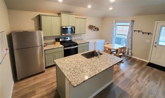 kitchen with appliances with stainless steel finishes, a sink, a kitchen island with sink, and light stone countertops