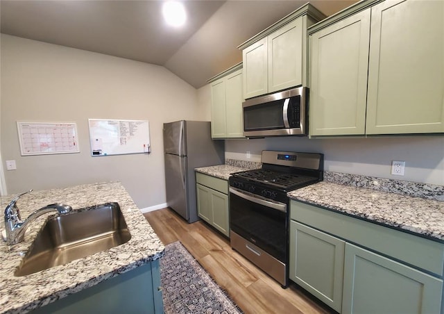 kitchen featuring lofted ceiling, a sink, light wood-style floors, appliances with stainless steel finishes, and green cabinetry