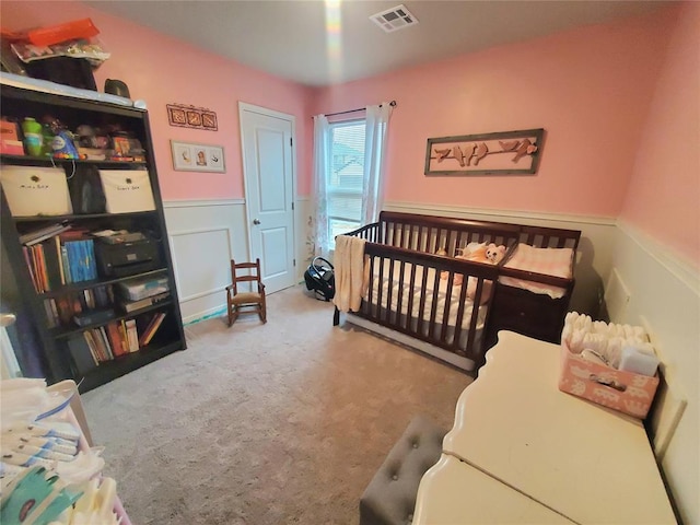 bedroom with light carpet, a wainscoted wall, visible vents, and a nursery area