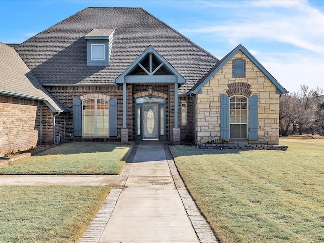 view of front facade with stone siding, a front lawn, roof with shingles, and brick siding