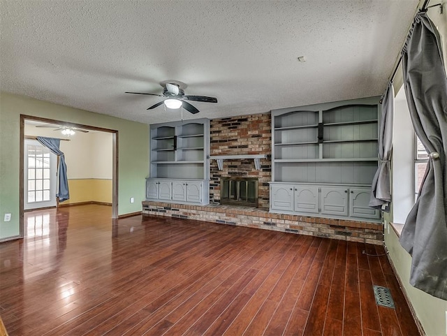 unfurnished living room with dark hardwood / wood-style floors, ceiling fan, a brick fireplace, a textured ceiling, and built in shelves