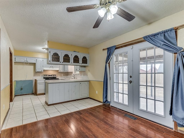 kitchen with a wealth of natural light, electric range, light hardwood / wood-style floors, kitchen peninsula, and french doors