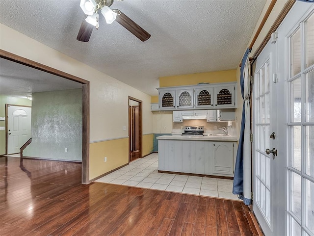 kitchen featuring sink, stainless steel range with electric stovetop, a textured ceiling, light wood-type flooring, and kitchen peninsula