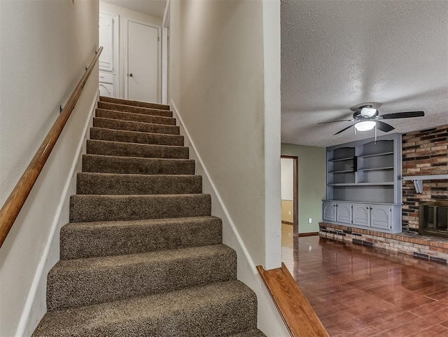 staircase featuring a textured ceiling, built in features, hardwood / wood-style flooring, ceiling fan, and a fireplace