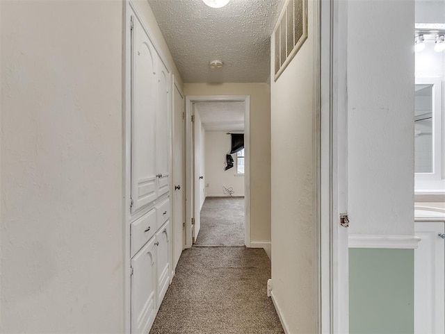 corridor with light carpet and a textured ceiling