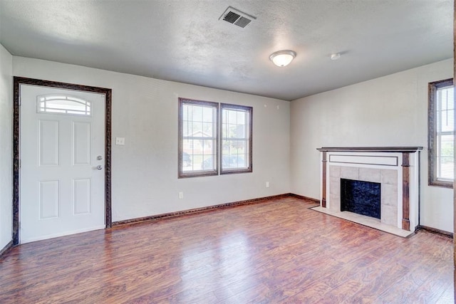 unfurnished living room with hardwood / wood-style flooring, a tile fireplace, and a textured ceiling