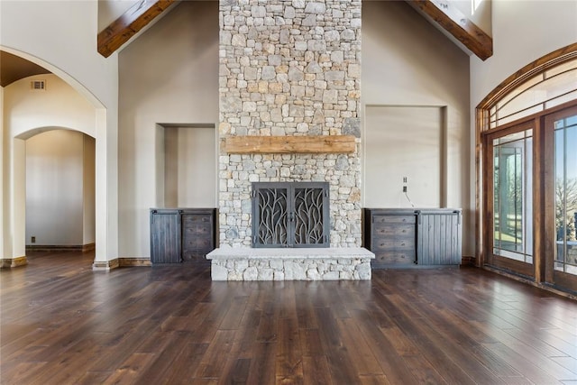 unfurnished living room featuring beamed ceiling, dark hardwood / wood-style floors, a stone fireplace, and high vaulted ceiling