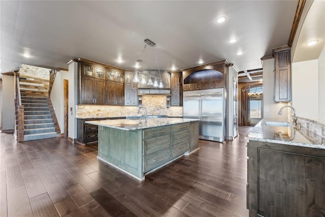 kitchen featuring pendant lighting, sink, a kitchen island with sink, light stone countertops, and built in fridge