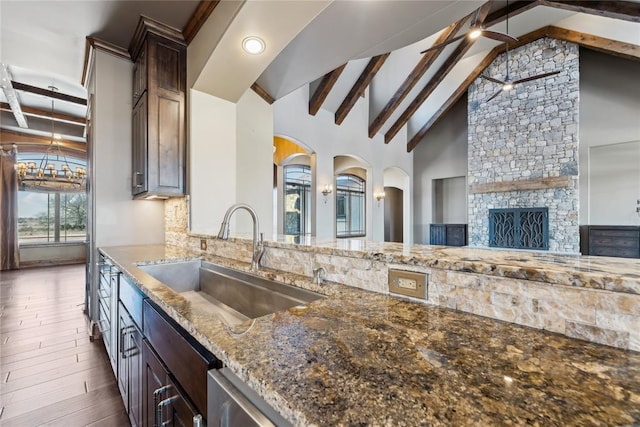 kitchen featuring sink, backsplash, beam ceiling, dark brown cabinetry, and stone countertops