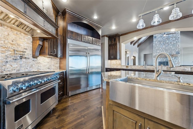 kitchen with sink, tasteful backsplash, light stone counters, premium appliances, and pendant lighting