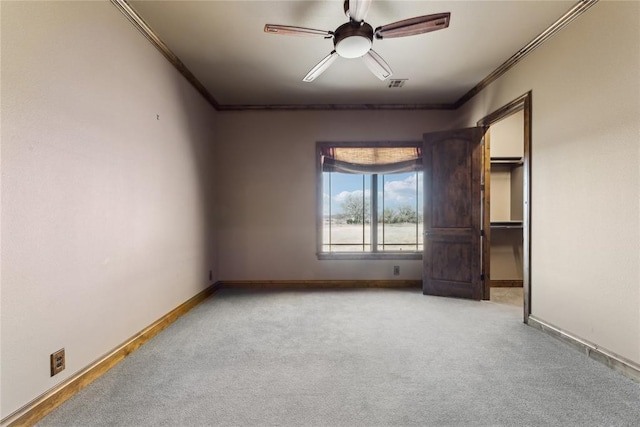 unfurnished bedroom with crown molding, ceiling fan, light carpet, and a walk in closet