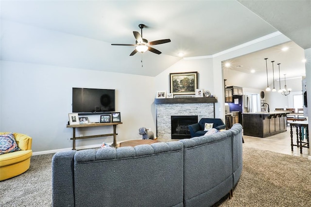 carpeted living room with sink, ceiling fan, ornamental molding, a stone fireplace, and vaulted ceiling