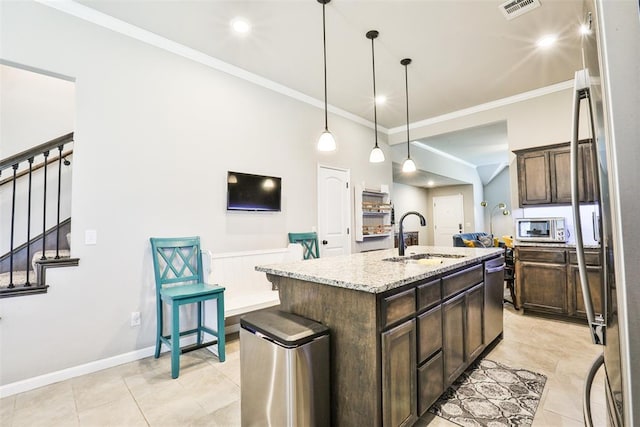 kitchen featuring pendant lighting, sink, dark brown cabinetry, light stone countertops, and an island with sink