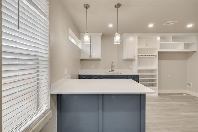 kitchen with sink, hanging light fixtures, light hardwood / wood-style floors, white cabinets, and kitchen peninsula