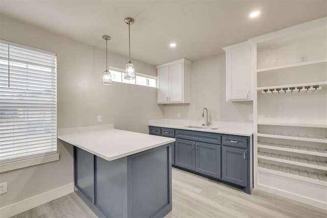 kitchen featuring sink, white cabinetry, light wood-type flooring, kitchen peninsula, and pendant lighting