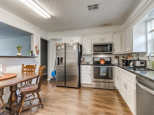 kitchen featuring dark stone countertops, appliances with stainless steel finishes, light hardwood / wood-style flooring, sink, and white cabinetry