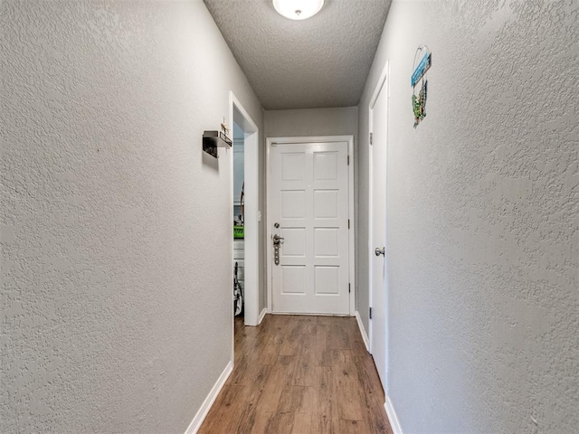 corridor with a textured ceiling and wood-type flooring