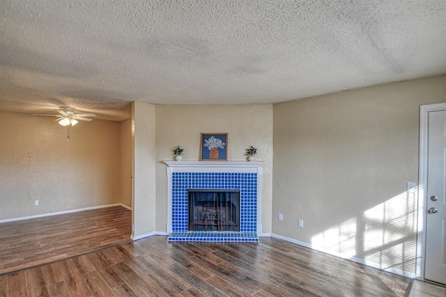 unfurnished living room featuring baseboards, a ceiling fan, wood finished floors, and a tiled fireplace