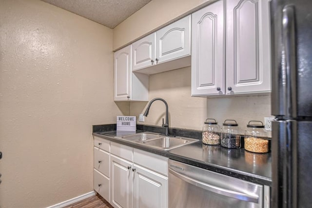 kitchen featuring a sink, freestanding refrigerator, a textured ceiling, white cabinetry, and stainless steel dishwasher