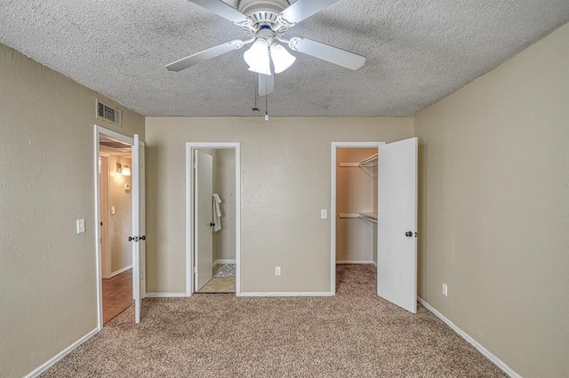 unfurnished bedroom featuring visible vents, a textured ceiling, ensuite bath, carpet floors, and a spacious closet