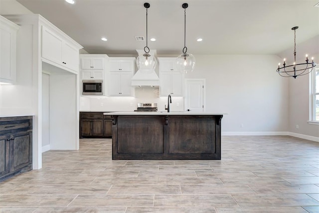 kitchen featuring built in microwave, sink, decorative light fixtures, and an island with sink