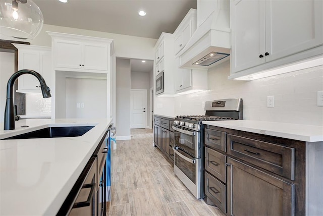 kitchen featuring sink, white cabinetry, stainless steel appliances, light stone countertops, and custom range hood