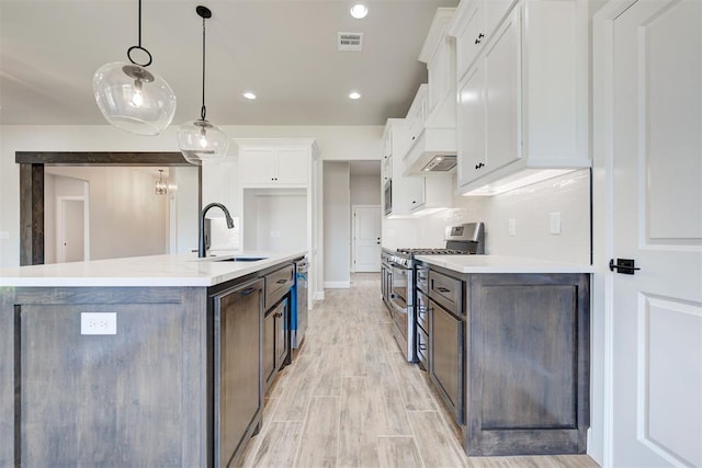 kitchen featuring sink, appliances with stainless steel finishes, hanging light fixtures, white cabinets, and a center island with sink