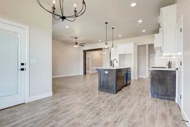 kitchen featuring white cabinetry, decorative light fixtures, a center island with sink, and light wood-type flooring