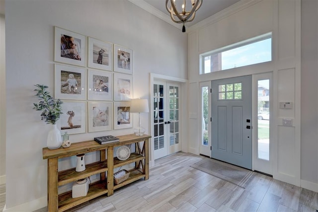 foyer entrance with crown molding, a towering ceiling, a chandelier, and light wood-type flooring