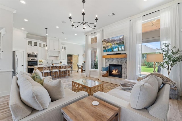 living room featuring crown molding, a tiled fireplace, a chandelier, and light wood-type flooring