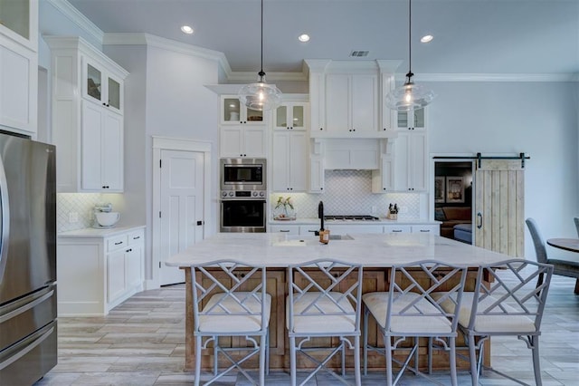 kitchen featuring hanging light fixtures, appliances with stainless steel finishes, a kitchen island with sink, and a barn door