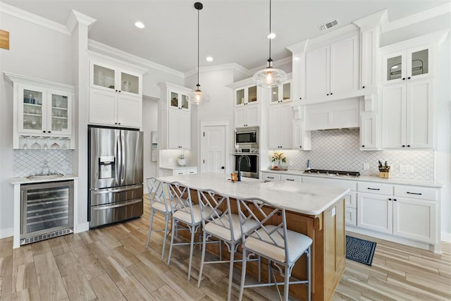 kitchen featuring decorative light fixtures, an island with sink, beverage cooler, light stone counters, and stainless steel appliances